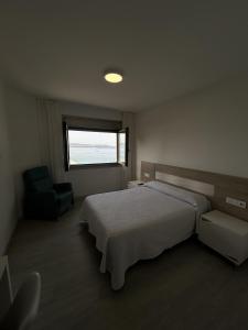 a bedroom with a bed and a chair and a window at Habitaciones A Postiña in Areas