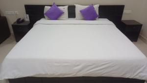 a large white bed with purple pillows on it at Hotel Tamilnadu Trichy in Tiruchirappalli