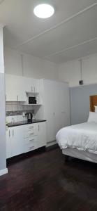 a white bedroom with a bed and a kitchen at Relax Guest House in Goodwood
