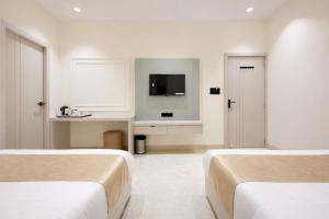 two beds in a white room with a tv at Sharda Grand in Ujjain