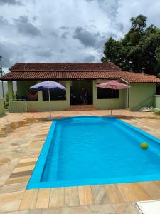 a blue swimming pool with two umbrellas in front of a house at Chácara Angola in Andradas