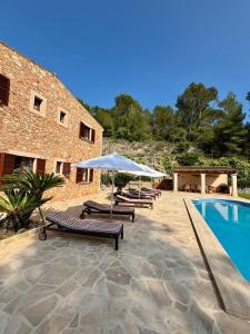 a pool with lounge chairs and an umbrella next to a building at Finca Es Puig, rustic estate with views in Es Carritxo