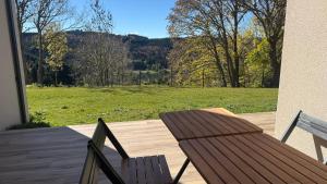 a wooden table and chairs on a deck with a view of a field at La Rose du Lac Hôtel Appart' in Coucouron