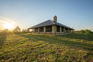 a house on a field with the sun setting behind it at Hilltop Bastrop Retreat in Bastrop