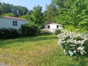a yard with a house and a bush with white flowers at Camping Onlycamp Les Peupliers du Lac in Chindrieux