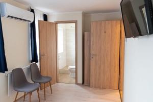 a bathroom with a toilet and two chairs and a television at Randevú Panzió in Sopron