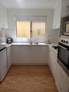 a white kitchen with a sink and a window at G & R Beach Cottage in Warnbro +7 photos