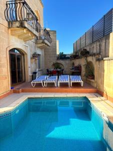 a swimming pool with two blue chairs next to a building at Ta Carmen Farmhouse with pool in Qala