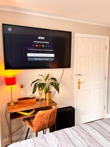 a bedroom with a desk with a television on the wall at Chrysanthemum Drive stays in Shinfield