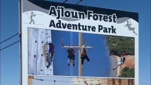 Ein Schild mit der Aufschrift „Abenteuerpark im Wald“ mit Leuten an einer Kletterwand in der Unterkunft Oak Chalet in Umm al Manābī‘