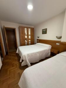 a bedroom with two beds with white sheets and wooden floors at Pensión Mencia in Lugones +3 photos
