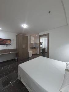 a bedroom with a large white bed and a kitchen at Lindo Flat Completo 311 in Nova Iguaçu