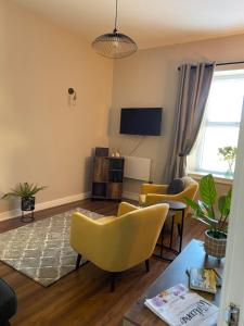 a living room with yellow chairs and a tv at Warm Spacious apartment in Pembroke Dock