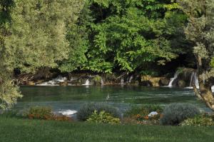 a river with trees and flowers and a waterfall at Kuća za odmor Komić in Smrdan