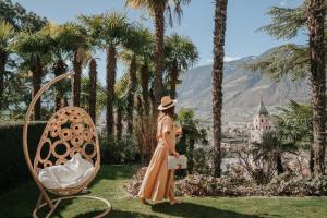 a woman in a dress and hat standing next to a chair at Villa Hochland in Merano