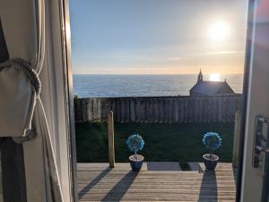 an open door with two potted plants looking out at the ocean at Allibella Shepherds Hut, Amazing Seaview, Private garden, Pet Friendly in Barmouth