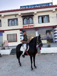 a man riding a black horse in front of a building at Hotel om banna in BhÄdura
