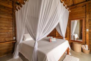 a bedroom with a white canopy bed with a mirror at Pousada D'Oxum Caraíva in Caraíva