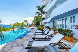 a row of chaise lounge chairs next to a swimming pool at Modern condo with ocean views, rooftop infinity pool & central AC in Puerto Vallarta