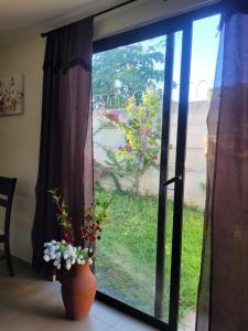 a vase with flowers in front of a window at Los Senderos in San Juan Opico