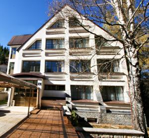 a white building with a tree in front of it at Hotel Fersped in Mavrovo