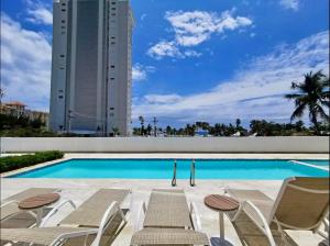 a swimming pool with chairs and a building at JUAN DOLIO 2BR Beach front SALITRE across Club Hemingway in Juan Dolio
