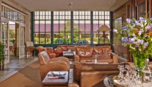 sala de estar con muebles de cuero y ventanas grandes. en Der Linslerhof - Hotel, Restaurant, Events & Natur en Überherrn