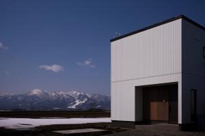 a white building with a door with mountains in the background at monel in Nakafurano
