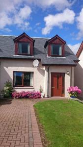 una casa bianca con porte rosse e fiori rosa di Holiday House Kinveachy ad Aviemore