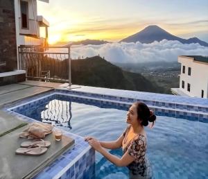 a woman standing next to a swimming pool with a view of a mountain at Lovia Villa Dieng in Kejajar
