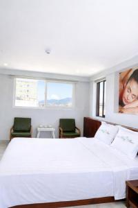 a bedroom with a large white bed with two chairs at Hồng Phúc 7 Hotel in Danang