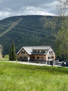 a large house in a field with a hill in the background at Apartmány Výsluní in Špindlerův Mlýn