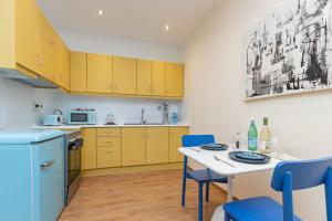 a kitchen with yellow cabinets and a table with blue chairs at Aila Stay in Corfu