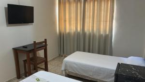 a room with two beds and a table and a television at Hotel San Remo in Ubá
