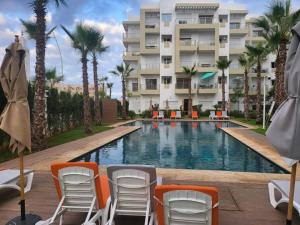 a swimming pool with chairs and a building at Superbe appartement à bouznika avec vue sur piscine et jardin privatif in Bouznika