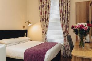ein Hotelzimmer mit einem Bett und einer Blumenvase in der Unterkunft Athena Hotel in London