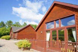 a log cabin with a fence and a house at Plum Tree Lodge in Errol