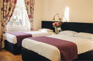 zwei Betten in einem Hotelzimmer mit Blumen auf einem Tisch in der Unterkunft Athena Hotel in London