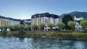 a building next to a river with trees and buildings at Hôtel Le Méditerranée in Lourdes