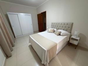 a white bedroom with a large white bed and a lamp at Vila dos Pinheiros 1 in Serra Negra