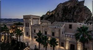 a building with palm trees in front of a mountain at Casa dalle valli del castello in Ioppolo Giancaxio