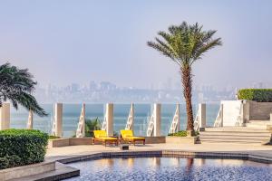 a swimming pool with two chairs and a palm tree at The Oberoi Mumbai in Mumbai
