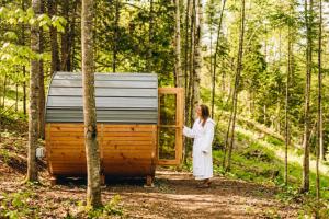 a woman standing in front of a tiny house in the woods at Chalet Gratitude with Private SPA & Sauna in Saint Come
