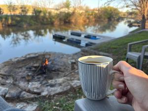 a person holding a cup of coffee next to a river at Lake Granbury House, Sleeps 11 with Lake Access! in Granbury