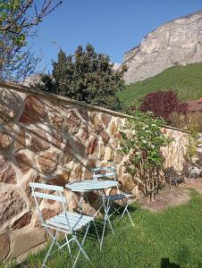 two chairs and a table in front of a stone wall at Cocon au pied de la Chartreuse in Lumbin