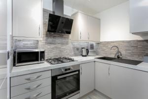 a white kitchen with white cabinets and a microwave at Forbes Retreat - Donnini Apartments in Ayr