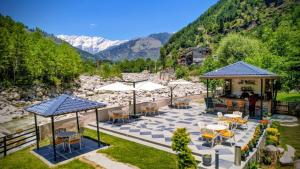 a patio with tables and umbrellas with mountains in the background at The Allure Grand - Riverside Resort & Spa in Manāli