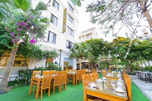 a restaurant with wooden tables and chairs in front of a building at Khách Sạn Melanta - FLC Sầm Sơn in Sầm Sơn