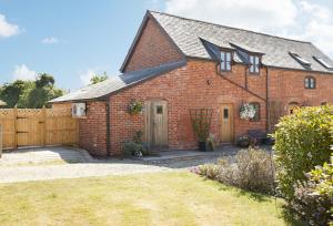 a red brick house with a wooden fence at Pear Tree Cottage Shropshire in Orleton