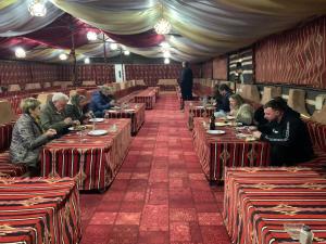 a group of people sitting at tables in a restaurant at Sand Rose Camp - Wadi Rum in Wadi Rum